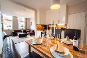 Ein modernes Wohnzimmer mit einer Couch, einem Esstisch für vier Personen und einer Küche im Hintergrund.