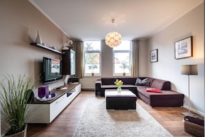 Un salon moderne avec un téléviseur à écran plat, un canapé, une table basse et une grande fenêtre avec des rideaux.