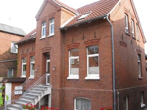 Um edifício de tijolos vermelhos com uma escadaria que leva a uma varanda, várias janelas e uma chaminé visível.