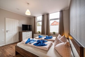 Ein Schlafzimmer mit zwei Betten, einem Fernseher, einem Schminktisch und einem Fenster mit Vorhängen.