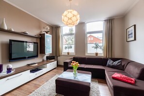Ein modernes Wohnzimmer mit Flachbildfernseher, braunem Sofa, Glastisch und einer dekorativen Vase mit Blumen.