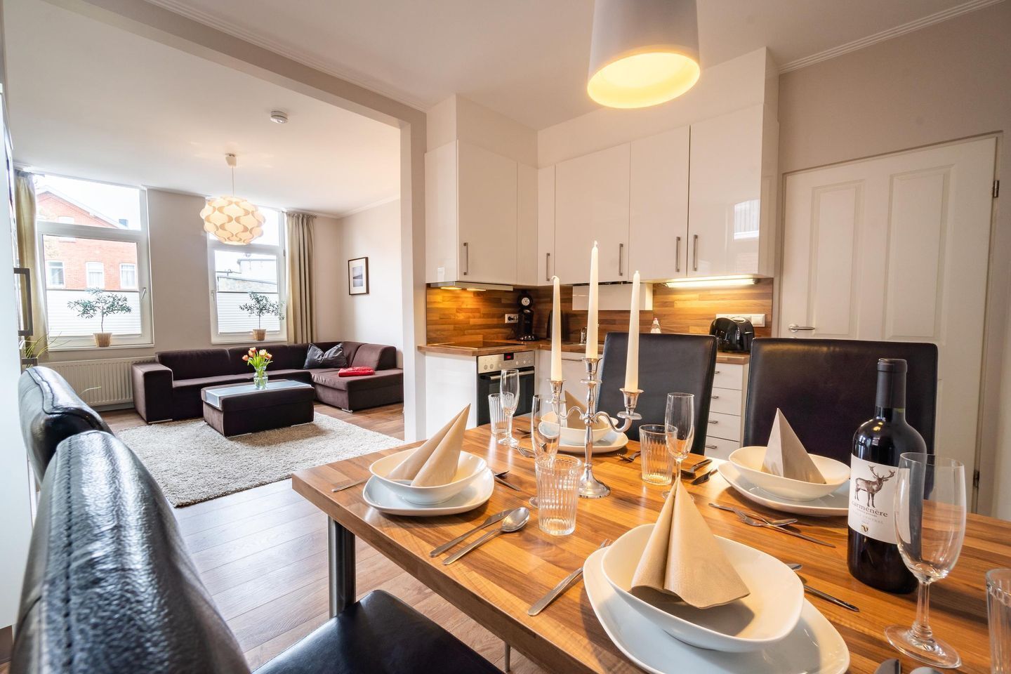 A modern living room with a sofa, a dining table set for four, and a kitchen in the background.