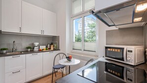 A modern kitchen with white cabinets, a black countertop, a round table with a bowl of fruit, and a microwave.