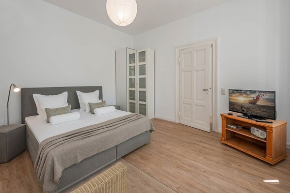 A bedroom with a bed, bedside table, lamp, TV, and a wooden TV stand.