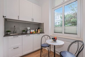 A modern kitchen with white cabinets, a marble countertop, a coffee maker, and a bowl of fruit on a small table.