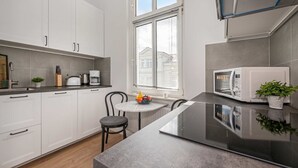 A modern kitchen with white cabinets, a black countertop, a dining table with chairs, and a microwave. - Charming vacation apartment in Heringsdorf, just 400 m from the beach - Villa (Heringsdorf)