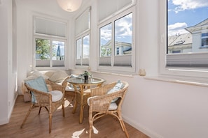 A room with wicker furniture, large windows, and a view of buildings outside.