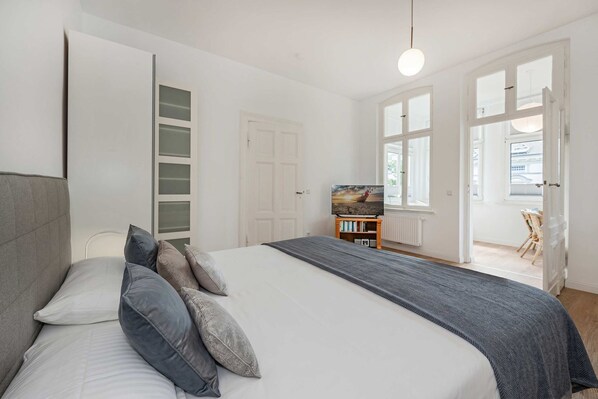 A bedroom with a bed, pillows, a TV, a bookshelf, and a view of the outside.
