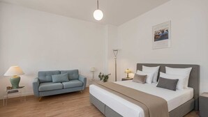 A bedroom with a bed, a grey sofa, a bedside table with a lamp, and a wall-mounted picture. - Charming vacation apartment in Heringsdorf, just 400 m from the beach - Villa (Heringsdorf)
