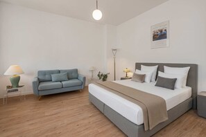 A bedroom with a bed, a grey sofa, a bedside table with a lamp, and a wall-mounted picture. - Charming vacation apartment in Heringsdorf, just 400 m from the beach - Villa (Heringsdorf)