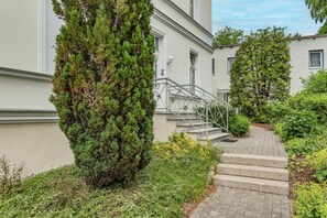 A residential building with a staircase leading to the entrance, surrounded by greenery and a paved pathway. - Charming vacation apartment in Heringsdorf, just 400 m from the beach - Villa (Heringsdorf)