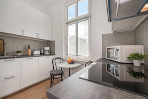 A modern kitchen with white cabinets, a black countertop, a dining table with chairs, and a microwave.