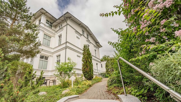 A building with a staircase leading to a door, surrounded by greenery and a metal railing. - Charming vacation apartment in Heringsdorf, just 400 m from the beach - Villa (Heringsdorf)