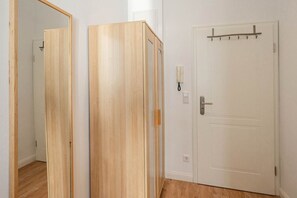 Una habitación con un armario de madera, una puerta blanca con un perchero y un interruptor de luz.