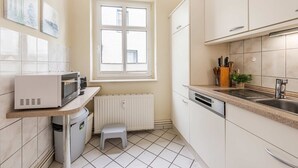 A compact kitchen with white cabinets, a built-in microwave, a window, and a small stool.