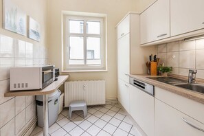 Una cocina compacta con armarios blancos, microondas integrado, una ventana y un taburete pequeño.