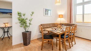 A dining area with a wooden table, chairs, a potted plant, a lamp, and a painting on the wall.