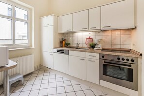 A kitchen with white cabinets, a built-in oven, a countertop with a coffee maker, and a window with blinds.