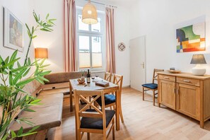 A cozy living room with a wooden dining table, chairs, a sofa, a wooden cabinet, and a hanging light fixture.