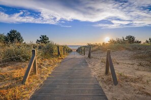 A wooden boardwalk leading to the beach, surrounded by sand and vegetation.