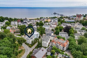 Une vue aérienne d’une ville côtière, avec un mélange de bâtiments résidentiels, une jetée s’avançant dans la mer et un hôtel imposant doté d’un toit rouge.