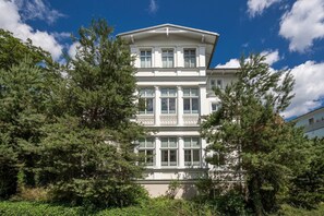 A multi-story building with large windows and a balcony, surrounded by trees.