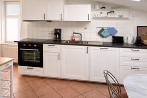 A modern kitchen with white cabinets, a black stove, a sink, and a countertop with various appliances. - Spacious apartment in Heringsdorf with 2 bathrooms, just 300 m from the beach - (Heringsdorf)