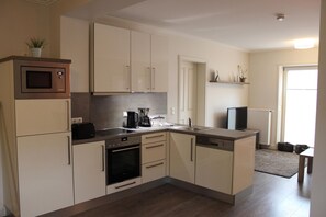 Una cocina compacta con armarios blancos, microondas, cafetera y lavavajillas.