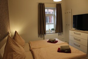Un dormitorio con cama, televisión, cómoda y ventana con cortinas.