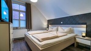 A modern bedroom with a large bed, bedside tables, a TV, and a window with curtains. - Altstadt Borkum Apartment 4 Bant - Altstadt Villa Borkum (Borkum)
