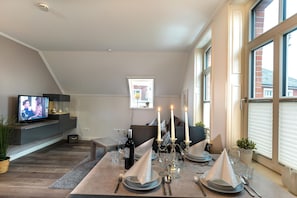 A modern living room with a television, dining table set for four, and a fireplace. - Altstadt Borkum Apartment 4 Bant - Altstadt Villa Borkum (Borkum)