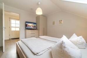 Un dormitorio con dos camas, un televisor sobre un mueble bajo, una lámpara colgante y una puerta que da a otra habitación.