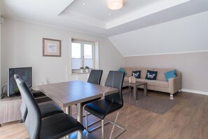 Ein modernes Wohnzimmer mit einem Holzesstisch, schwarzen Stühlen, einer blauen Couch und einem Fernseher.