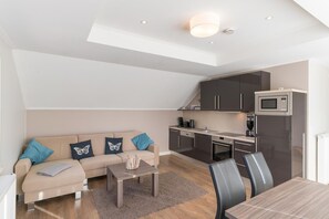 Un espacio habitable compacto con sofá, una mesita de centro y una mesa de comedor. Incluye una kitchenette con microondas y horno.