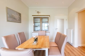 A dining room with a wooden table and six chairs, a window with a view, and a door leading to another room.