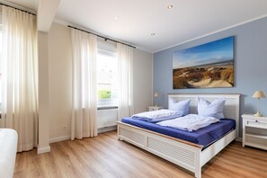 Una camera da letto con un letto, un comodino, una lampada, una finestra con tende e un quadro appeso al muro.