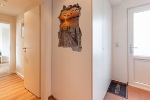 Un couloir avec une porte, un paillasson et un mur orné d’une œuvre d’art à la texture particulière.