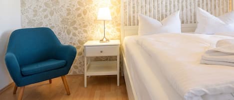 A bedroom with a bed, a nightstand with a lamp, a chair, and a wall with a floral pattern.