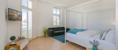 Una habitación moderna con una cama, un sofá, un televisor y una pequeña mesa con una planta.