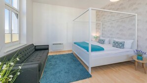 A bedroom with a four-poster bed, a sofa, a small round table, and a window. - Apartment Karlskrona in Ahlbeck with balcony, close to the beach - Haus Skanska (Heringsdorf)