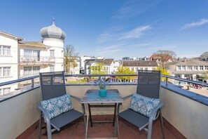 Un balcon avec deux chaises, une table et un vase de fleurs.