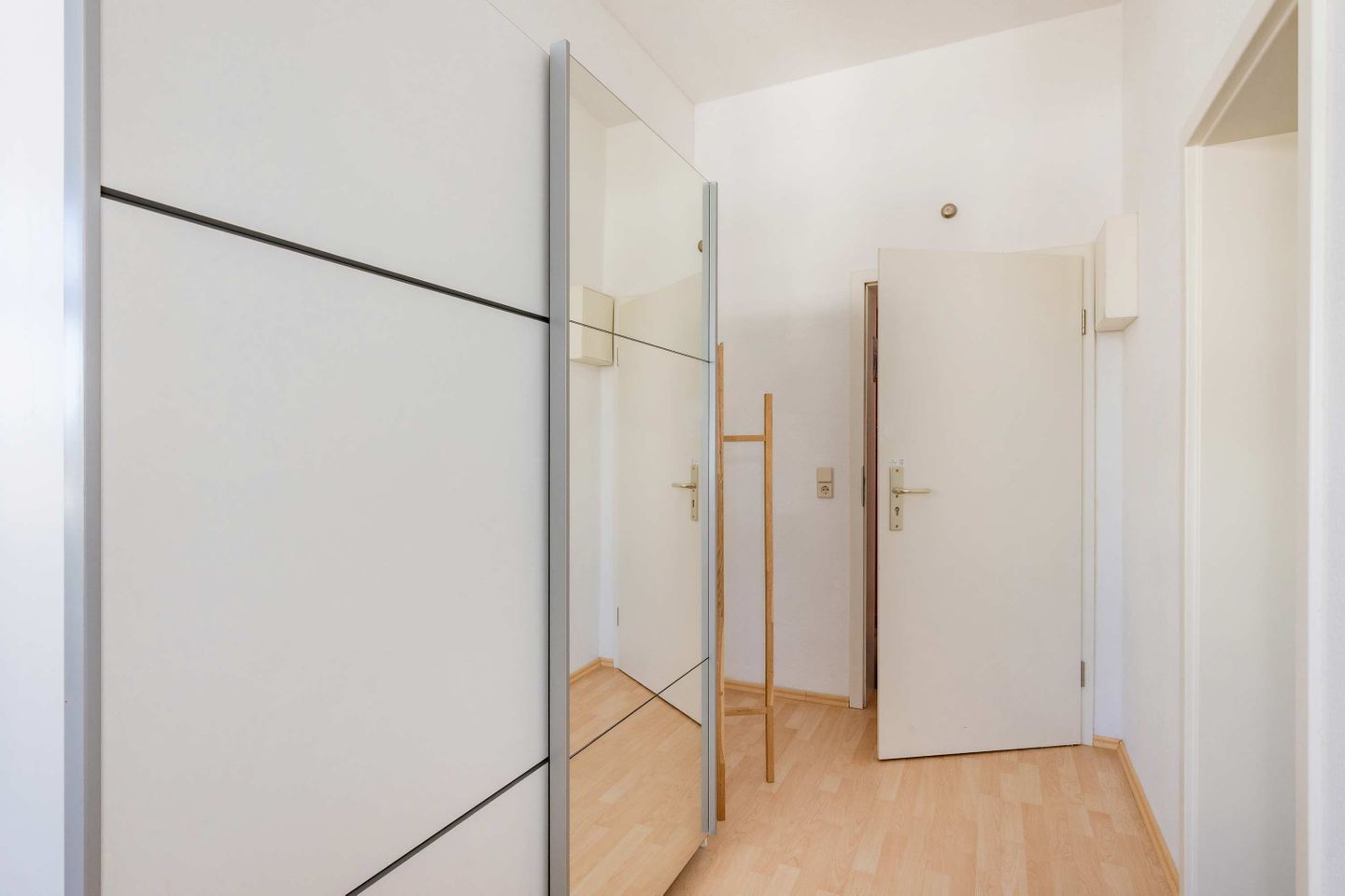 Ein Flur mit weißen Wänden, Holzboden und einem Spiegelkleiderschrank.