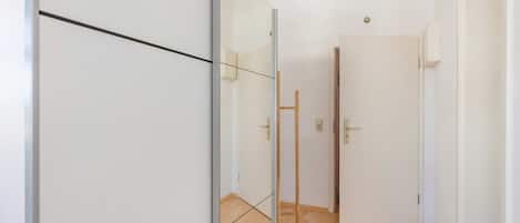 Ein Flur mit weißen Wänden, Holzboden und einem Spiegelkleiderschrank.
