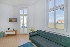 A modern living room with a green sofa, a wooden cabinet, a TV, and a sliding glass door leading to a balcony. - Apartment Karlskrona in Ahlbeck with balcony, close to the beach - Haus Skanska (Heringsdorf)