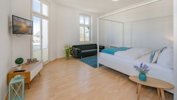 A modern room with a bed, a sofa, a TV, and a small table with a plant. - Apartment Karlskrona in Ahlbeck with balcony, close to the beach - Haus Skanska (Heringsdorf)