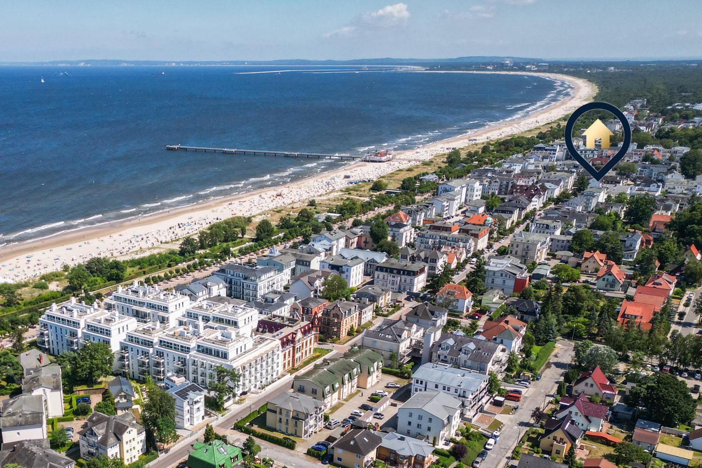 An aerial view of a coastal town with a beach, residential buildings, and a pier extending into the sea.