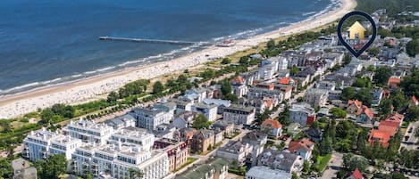 An aerial view of a coastal town with a beach, residential buildings, and a pier extending into the sea.