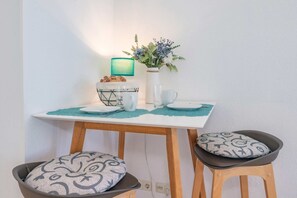 Pieni ruokailutila, jossa on pöytä, kaksi tuolia, maljakko kukkineen, leipäkori ja turkoosinvärinen lamppu.