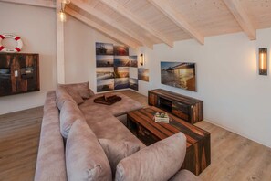 Un salon moderne avec un grand canapé d’angle, une table basse en bois et un téléviseur fixé au mur.