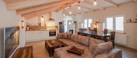 A spacious loft with exposed wooden beams, a large sofa, a dining area, and a kitchen with modern appliances.